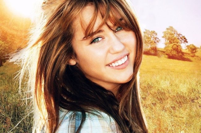Miley sorrindo em um campo e cabelos ao vento.
