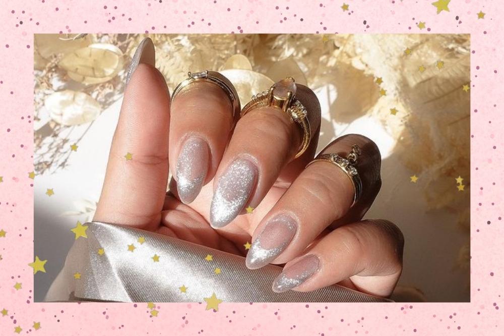 Montagem com o fundo rosa e detalhe de estrelas douradas com a foto de uma mão com as unhas longas e nail art com efeito aveludado com esmalte metalizado.