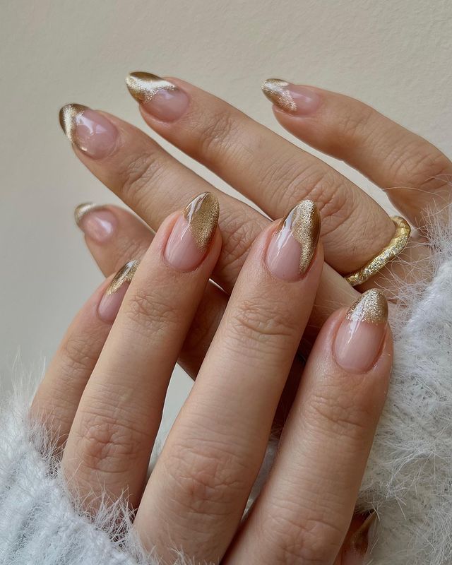 Foto de mãos com as unhas longas com nail art dourada com esmalte metalizado.