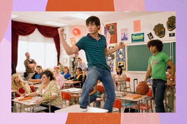 Zac Efron como Troy Bolton, de HSM, fazendo um sinal de forte com as mãos em cima de uma carteira na sala de aula