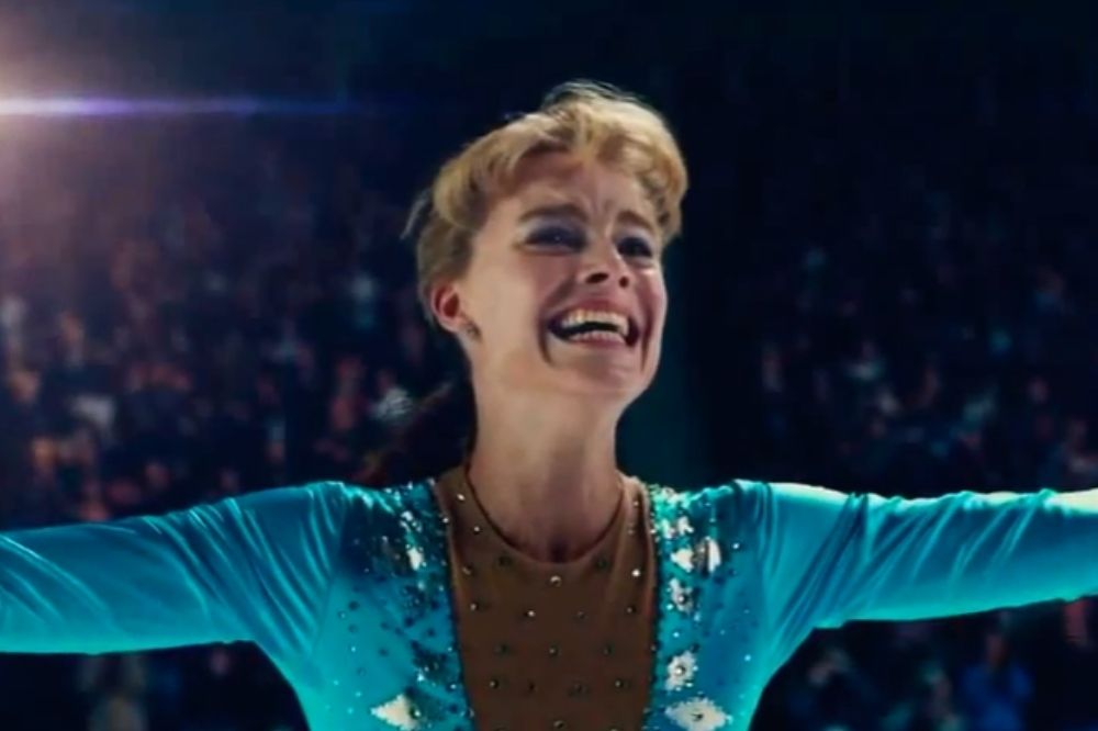 Margot Robbie como Tonya Harding sorrindo de braços abertos emocionada enquanto patina com figurino azul com detalhes brancos