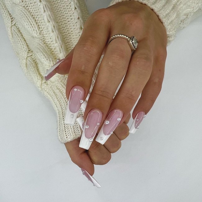 Foto de unhas longas com decoração de francesinha simples branca e aplicação de pérolas pequenas.