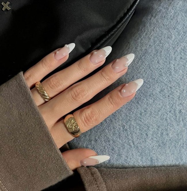Foto de uma mão com as unhas longas decoradas com uma francesinha branca clássica e aplicação de pérolas.