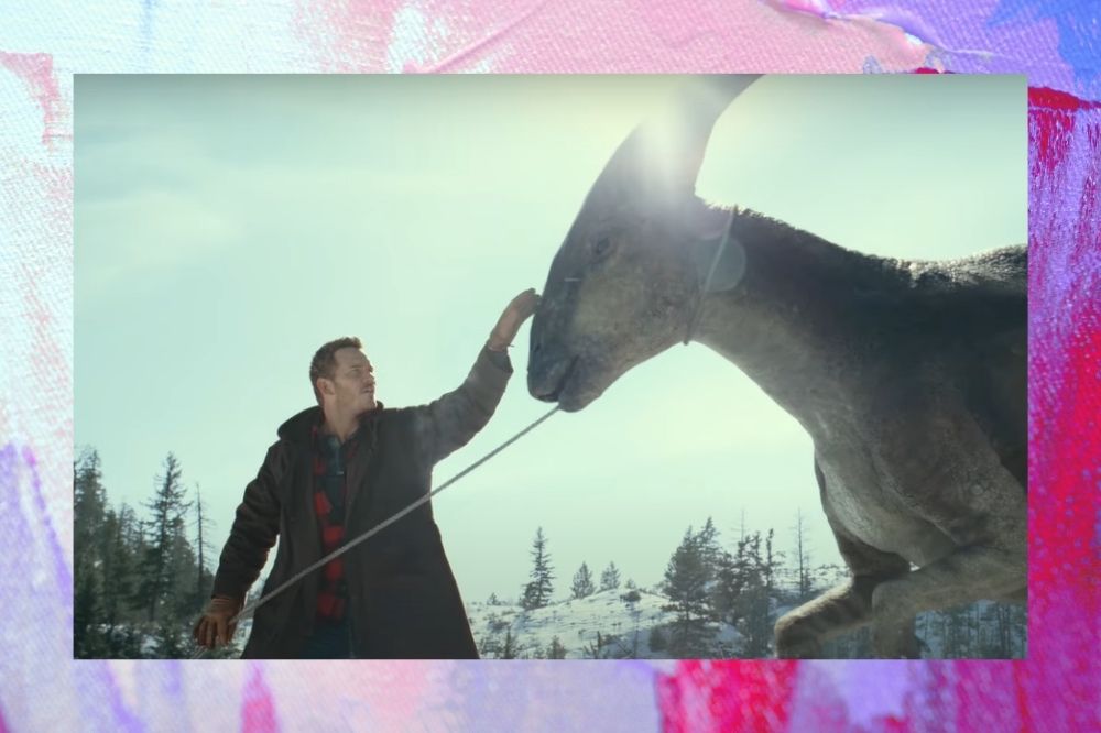 Chris Pratt com a mão na cabeça de um dinossauro ao ar livre.