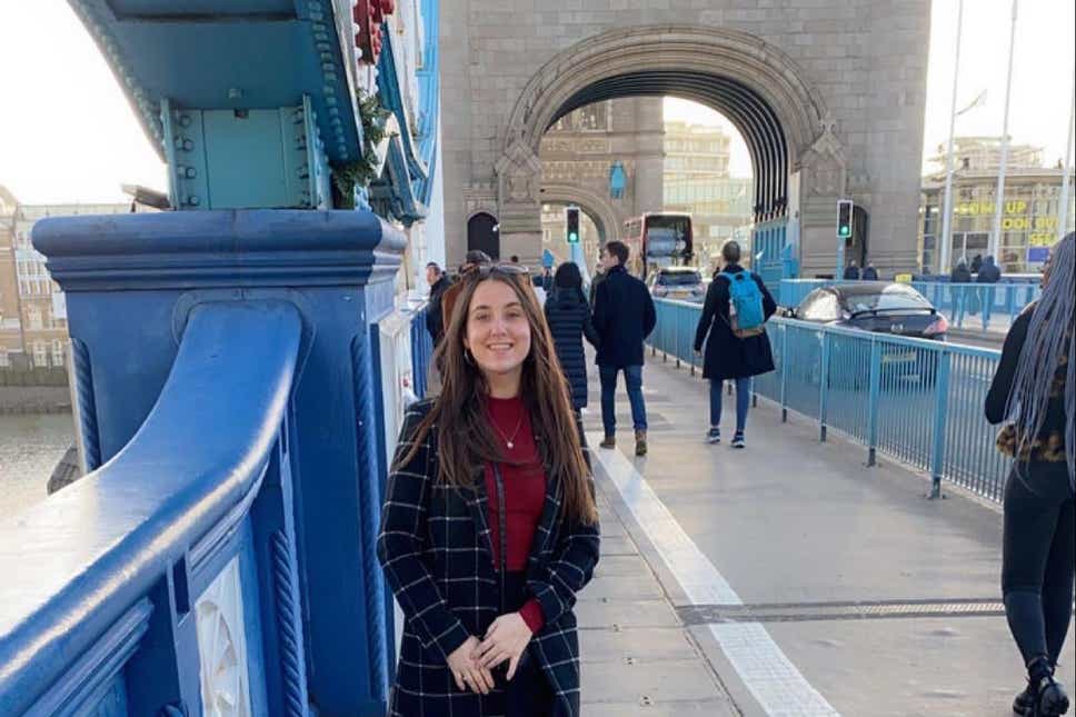 Foto da jovem Ashley Wadsworth na ponte da torre, na Inglaterra. Ela é alta, branca, cabelos castanhos e lisos.