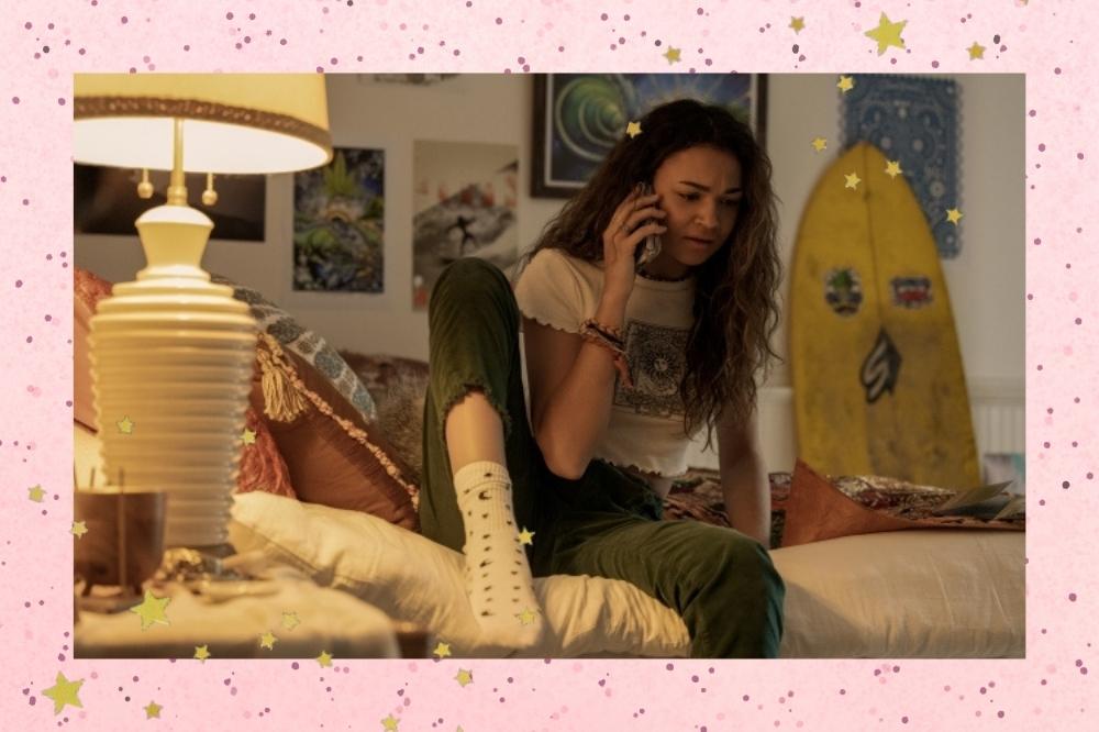 Montagem com o fundo rosa com detalhe de estrelinhas douradas nas bordas com foto da Madison Bailey como Kiara no quarto da personagem em cena de Outer Banks, série da Netflix