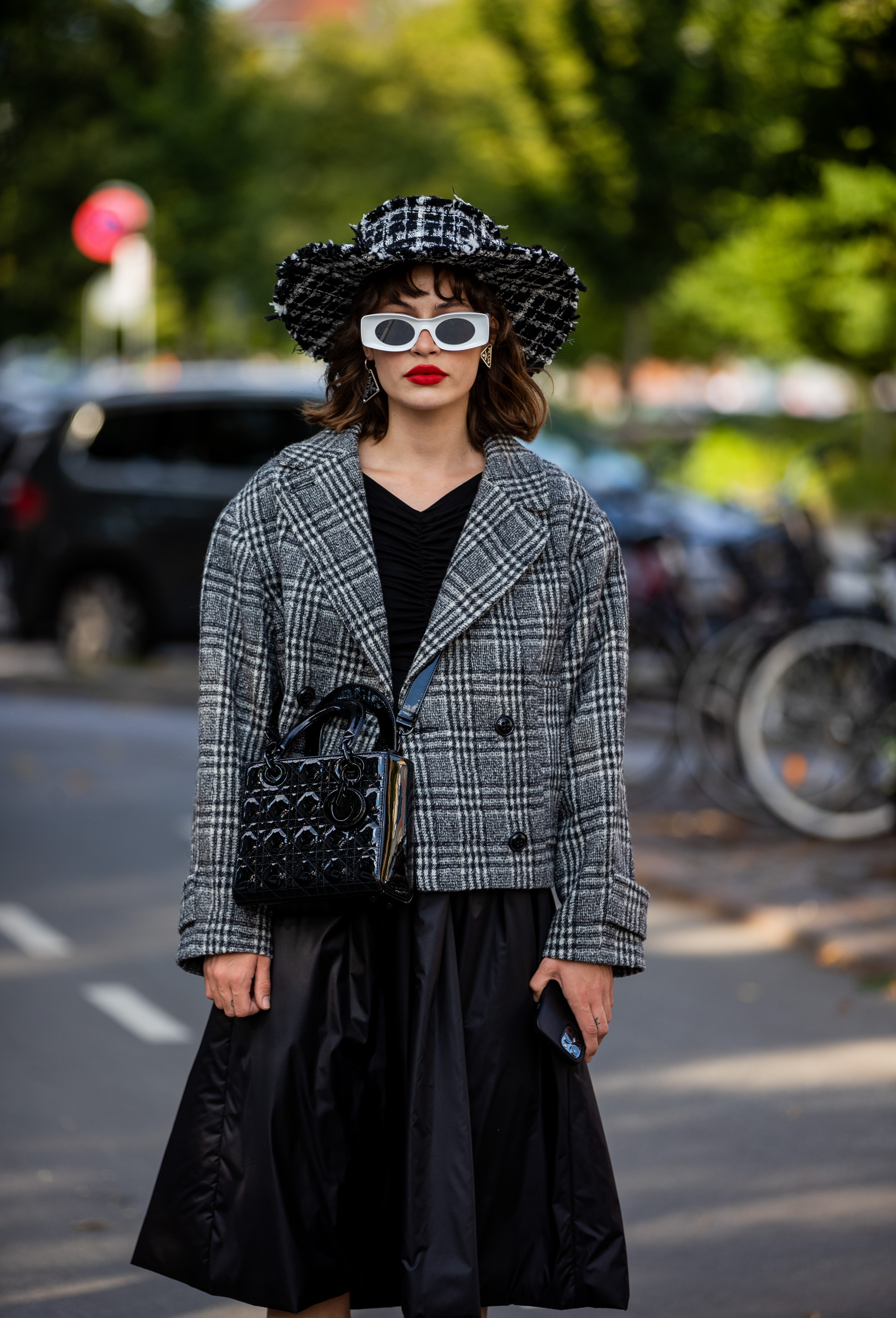 Lele Berlin na semana de moda de Copenhagen, na Dinamarca usando chapéu preto e branco, óculos de sol branco, vestido preto, blazer preto e branco e bolsa preta atravessada no corpo