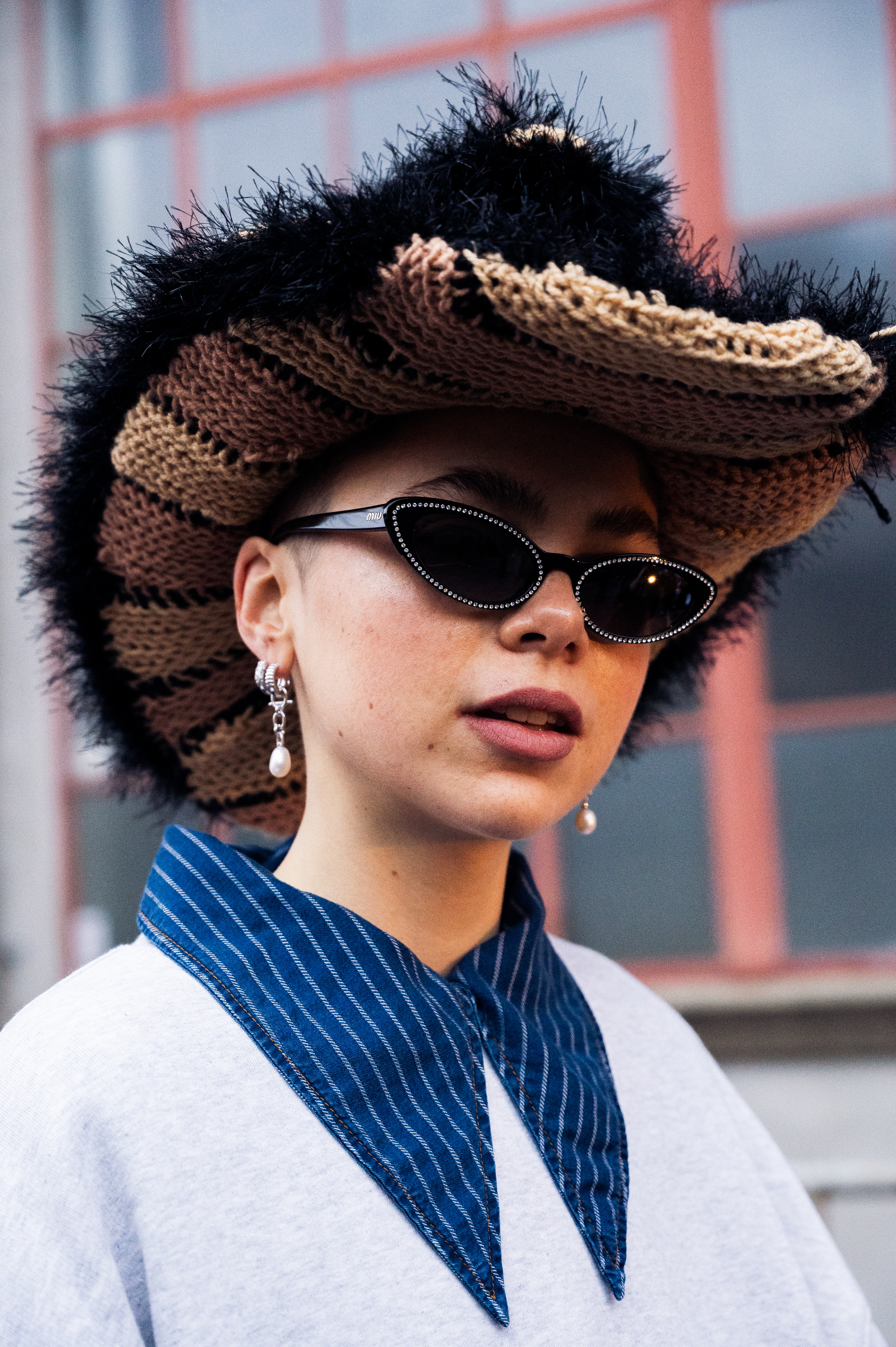 Emma Fridsell na semana de moda de Copenhagen usando chapéu cowboy, camisa listrada sobreposta a moletom branco, óculos de sol e brincos de pérolas