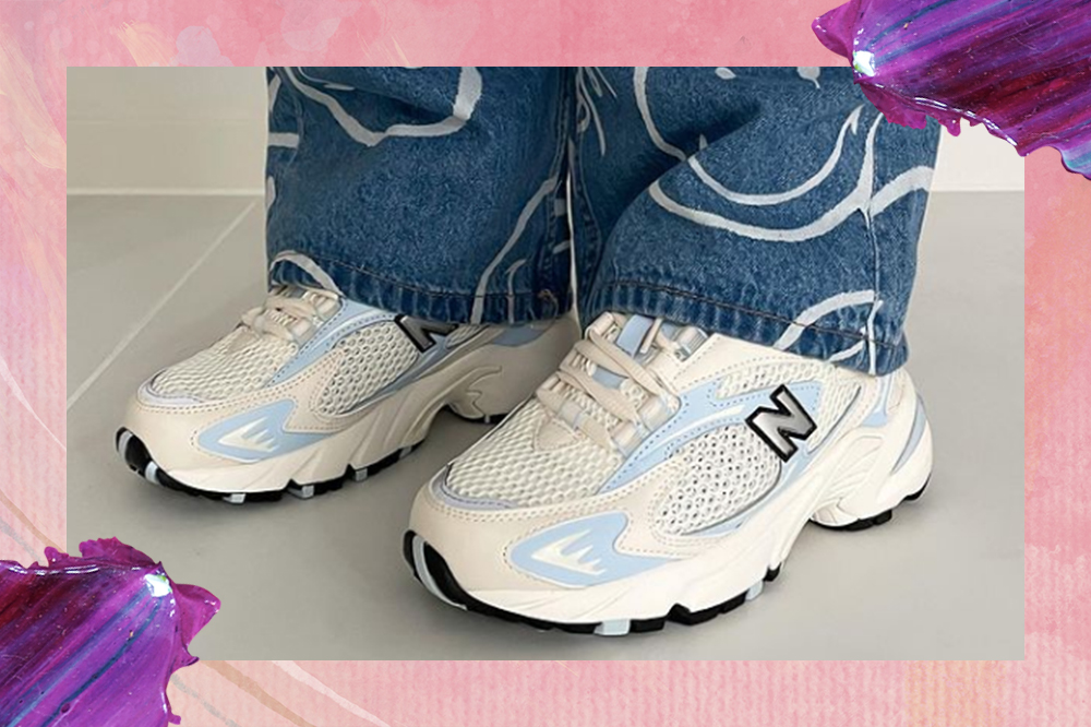 Montagem em fundo rosa com tintas em roxo nas laterais de foto que mostra pé usando tênis branco e azul da New Balance e parte da calça jeans