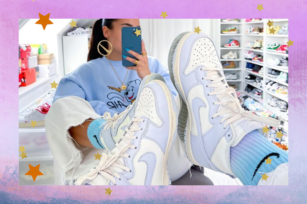 Garota usando moletom azul, calça branca e tênis azul com meia azul da Nike. Ela está com os pés em frente a um espelho, cobrindo seu rosto com o celular.