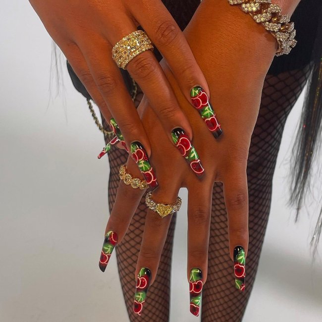 Foto das mãos da rapper Megan Thee Stallion com destaque para as unhas longas com decoração de desenho de cereja.