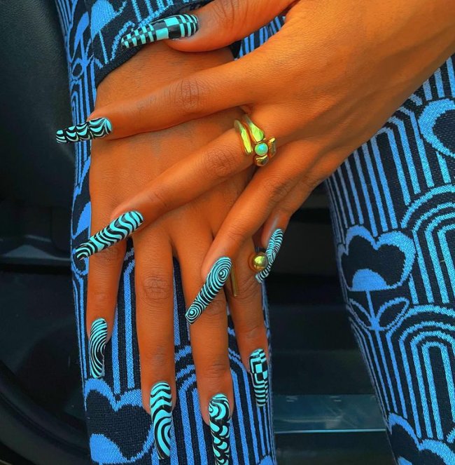 Foto das mãos da rapper Megan Thee Stallion com destaque para as unhas longas com decoração preta e branca em uma estampa psicodélica.