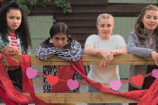 Quatro meninas encostadas em uma cerca decorada com corações.