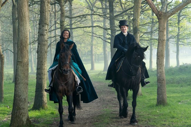 Simone Ashley como Kate Sharma e Jonathan Bailey como Anthony Bridgerton em cena de Bridgerton; eles estão andando de cavalo lado a lado em uma trilha na floresta enquanto sorriem