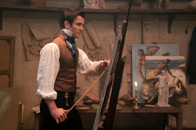 Luke Thompson como Benedict Bridgerton pintando um quadro com desenhos presos na parede ao fundo
