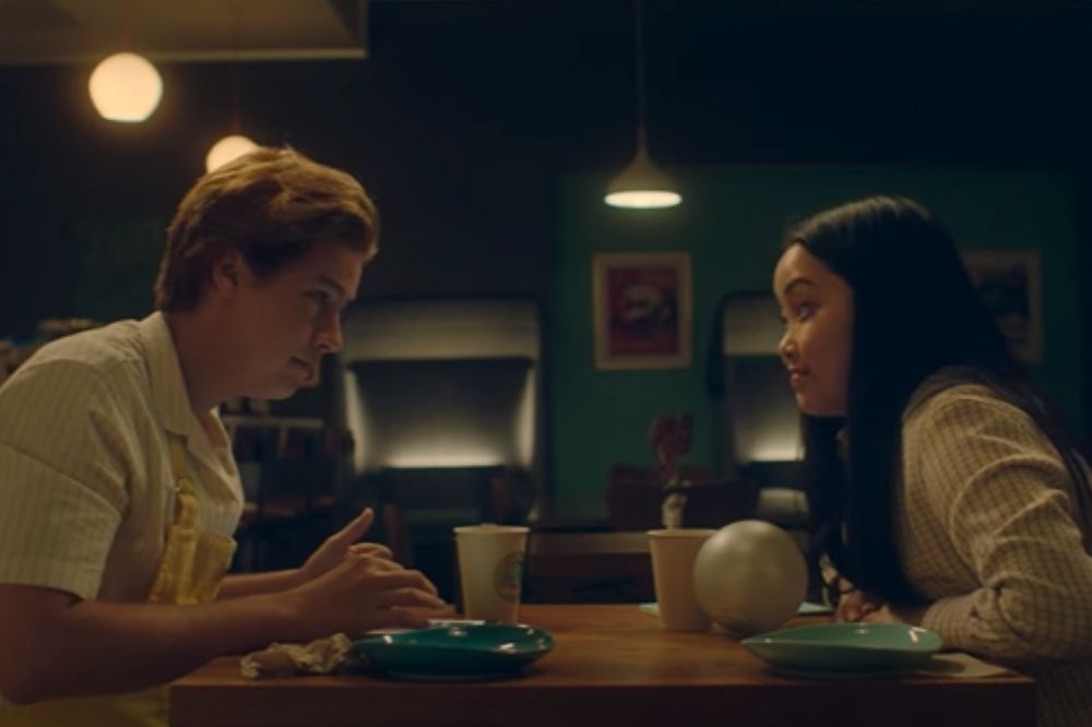 Cole Sprouse e Lana Condor em cena do trailer de Nossos Sonhos de Marte, filme da HBO Max; eles estão sentados em uma mesa de frente um para o outro e se olhando