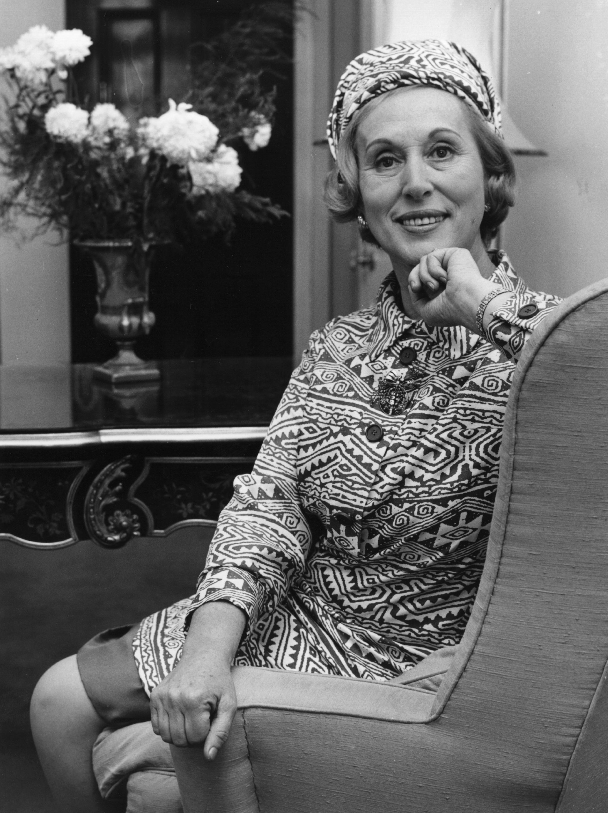 A empreendedora Estée Lauder sorrindo e olhando para a câmera sentada em uma cadeira