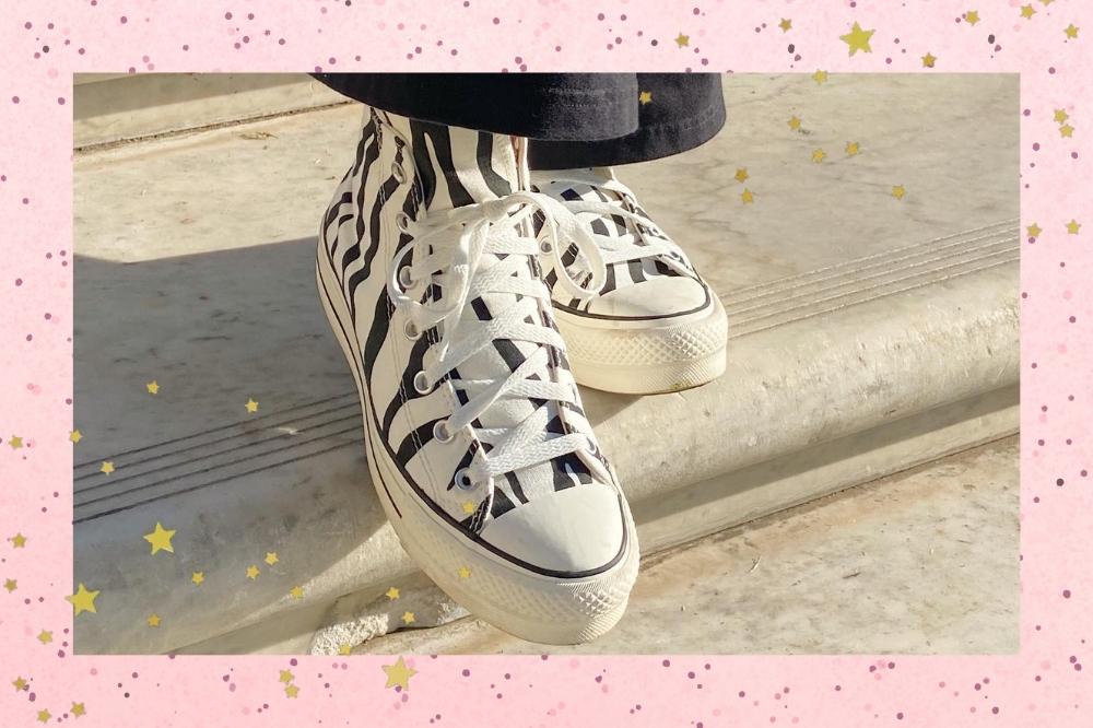 Montagem com o fundo rosa com e detalhes de estrelas douradas nas bordas com a foto de um tênis Converse de cano alto e estampa de zebra.
