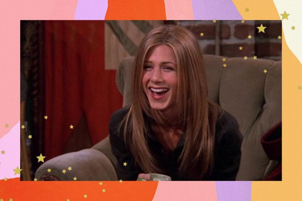 Montagem com o fundo colorido e detalhes de estrelinhas douradas nas bordas com a foto da personagem Rachel Green de Friends. Na foto ela está com o cabelo solto com corte em camadas, blusa preta, olha para frente e sorri.