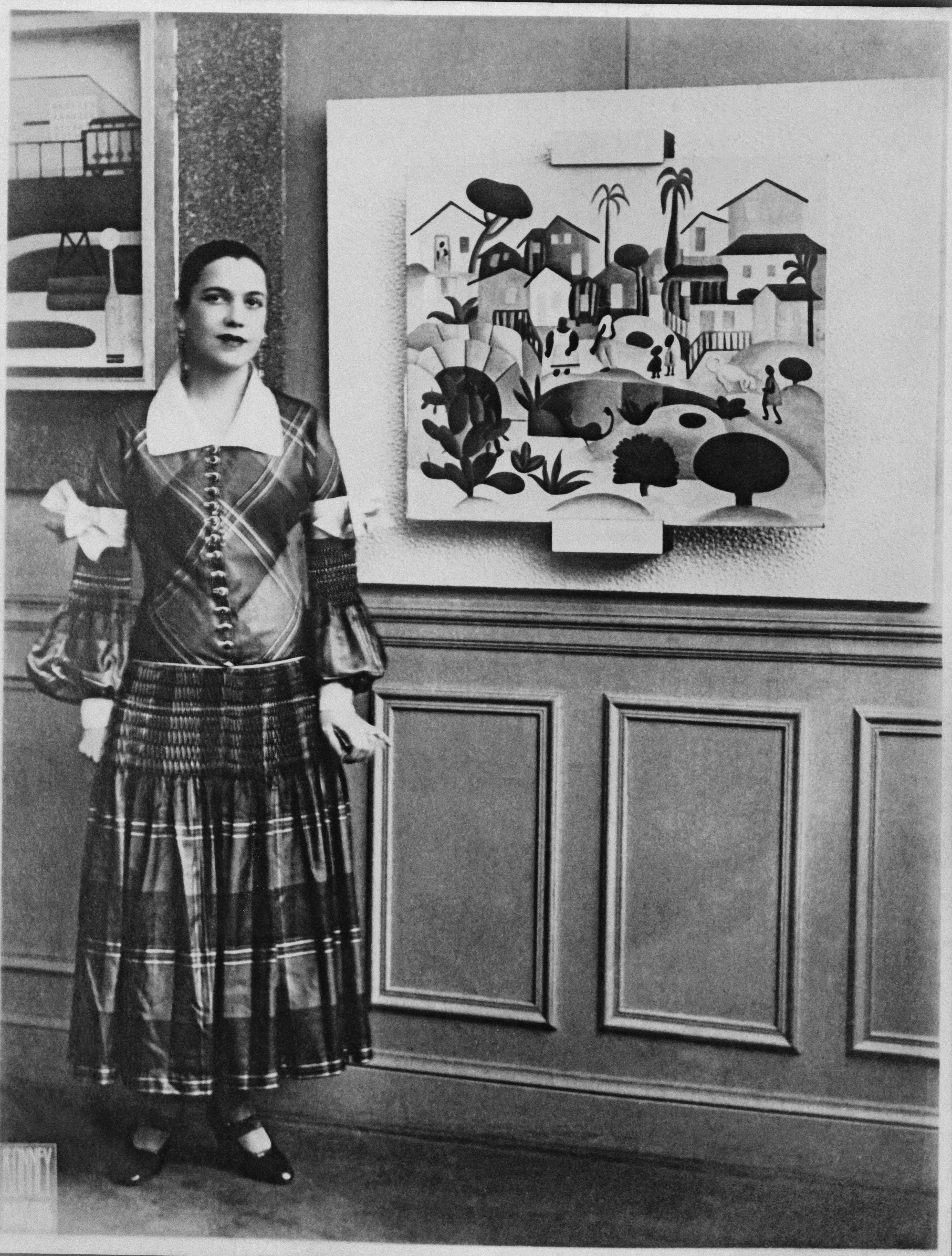 Tarsila do Amaral com vestido xadrez da maison Paul Poiret ao lado de seu quadro 