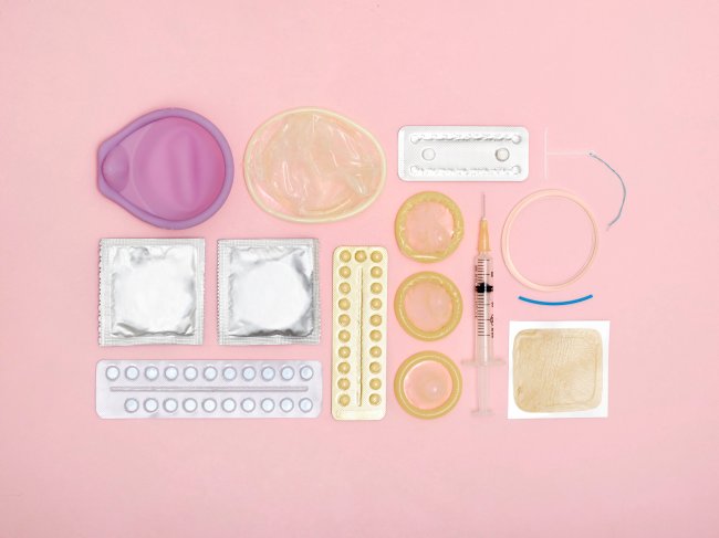 Foto de Métodos contraceptivos espalhados em um fundo rosa.