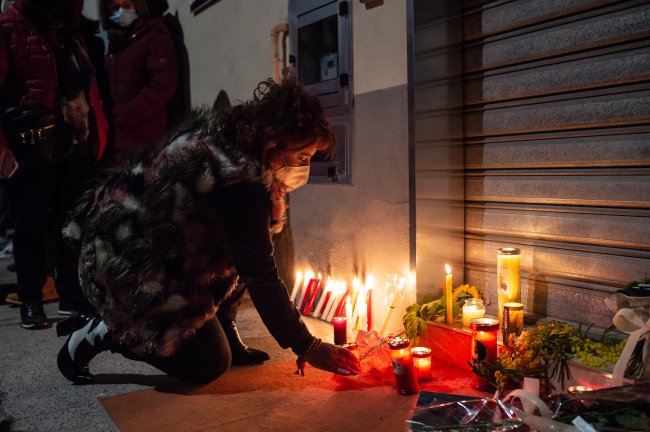 Foto de uma mulher ajoelhada acendendo uma vela em um memorial feito para uma mulher vítima de feminicídio. Está de noite.