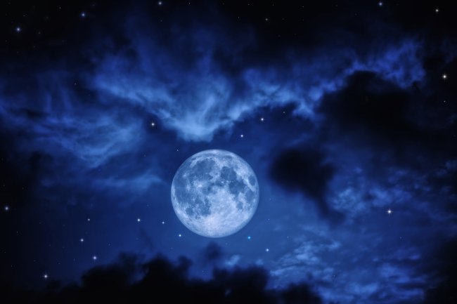 Foto de uma lua cheia em um céu azul bastante nublado e com estrelas. Imagem tem um ar angustiante.