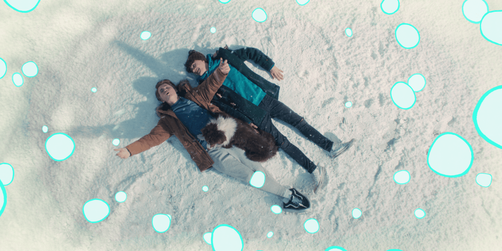 Nick, Charlie e Nellie de Heartstopper deitados na neve; a imagem é vista por cima e efeitos de neve animados ilustrados ao redor da cena da adaptação