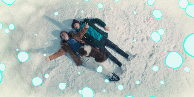 Heartstopper_Season1_Episode2_00_14_52_02 Nick, Charlie e Nellie de Heartstopper deitados na neve; a imagem é vista por cima e efeitos de neve animados ilustrados ao redor da cena da adaptação