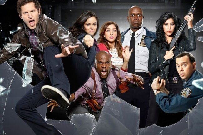 Foto promocional de Brooklyn 99 com os personagens quebrando um vidro de sala de interrogatório; eles fazem expressões de choque, assustadas e neutras