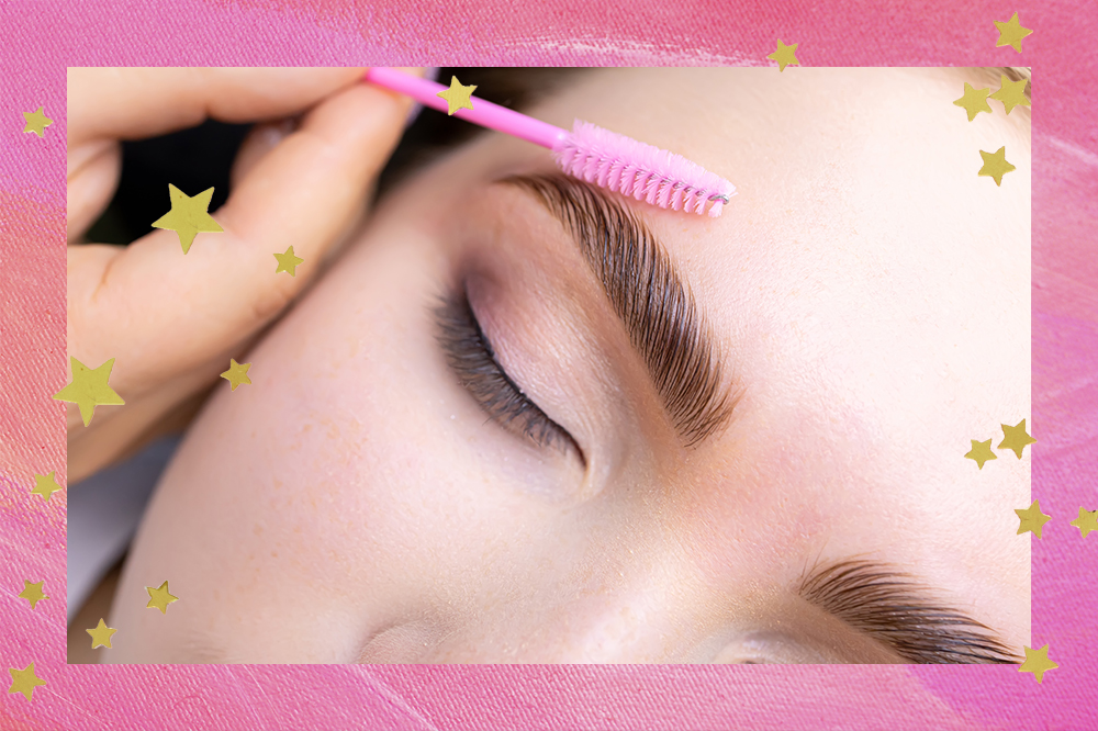 Garota de olhos fechados fazendo procedimento de brow lamination e com uma escovinha rosa penteando as sobrancelhas. O fundo da montagem é rosa com estrelinhas douradas