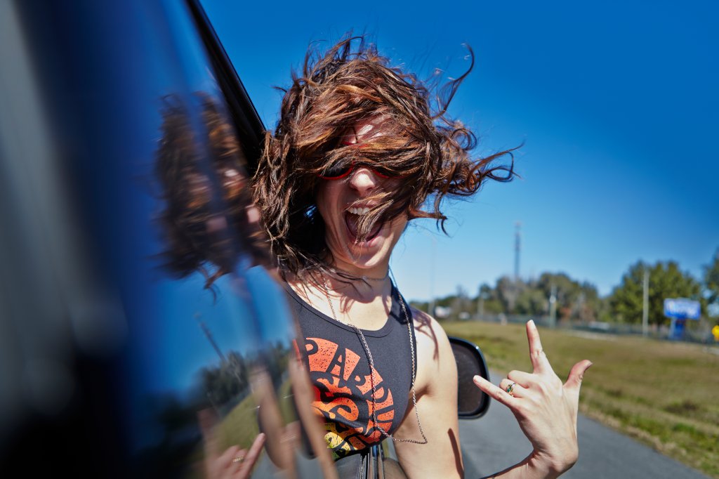 Mulher sorrindo com a cabeça pra fora da janela do carro em movimento