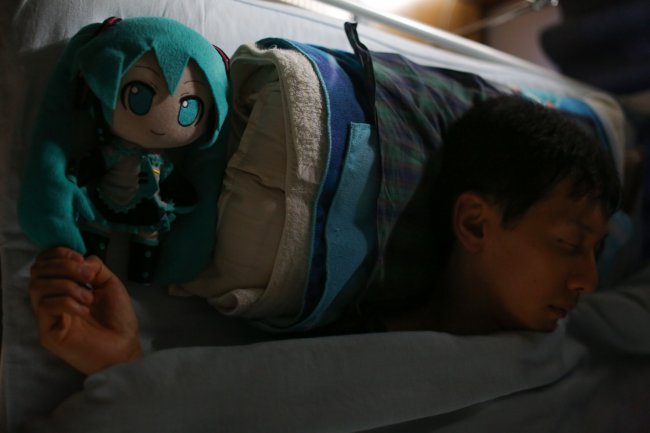 O japonês Akihiko Kondo dormindo em sua cama ao lado de uma boneca de pelúcia de cabelos azuis