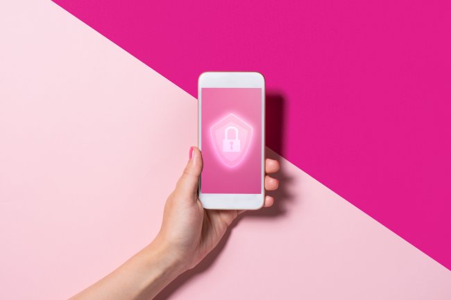 Uma mão segurando um celular com um cadeado na tela. O fundo da foto é rosa e pink