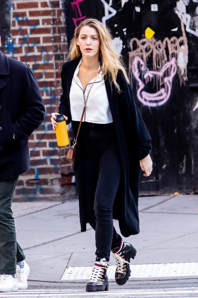 Foto da Blake Lively andando na rua. Ela usa uma camisa branca, casaco alongado preto e calça preta.