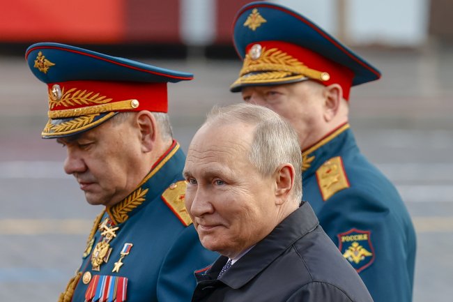 Vladimir Putin durante parada militar que aconteceu em maio de 2022. Ele veste um sobretudo preto, é um homem branco e com cabelo grisalho. Está cercado de soldados.