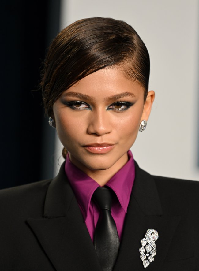 Foto da Zendaya na Vanity Fair de 2022 com um look com blazer e gravata e maquiagem com esfumado preto nos olhos. Ela olha para o lado e não sorri.