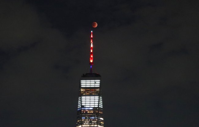Foto da Lua de Sangue brilhando avermelhada atrás de um prédio enorme