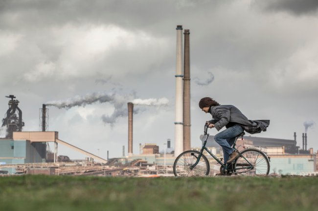 mulher pedala em frente a indústrias que estão soltando gases tóxicos