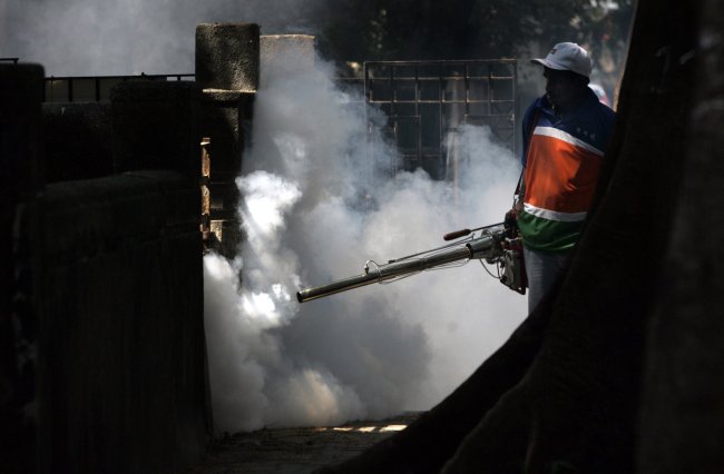 Foto de um homem segurando um equipamento que solta fumaça e mata mosquitos