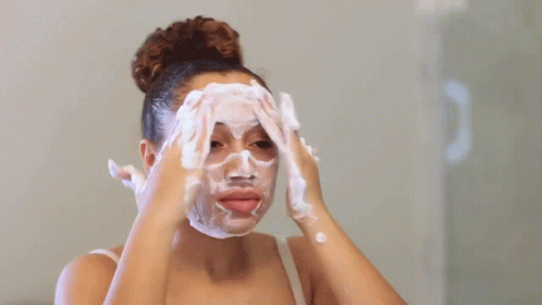 Garota lavando o rosto e fazendo movimentos circulares com as mãos para cuidar da pele