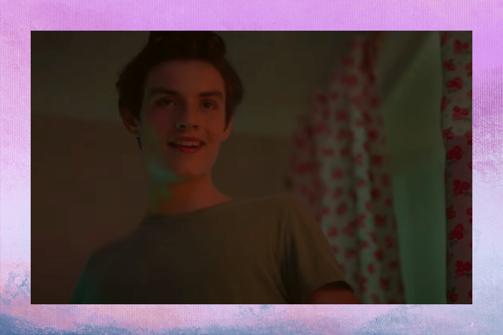 Louis Partridge sorrindo em cena de filme em que interpreta Peter Pan; a margem é uma textura nas cores azul, rosa, roxo e branco