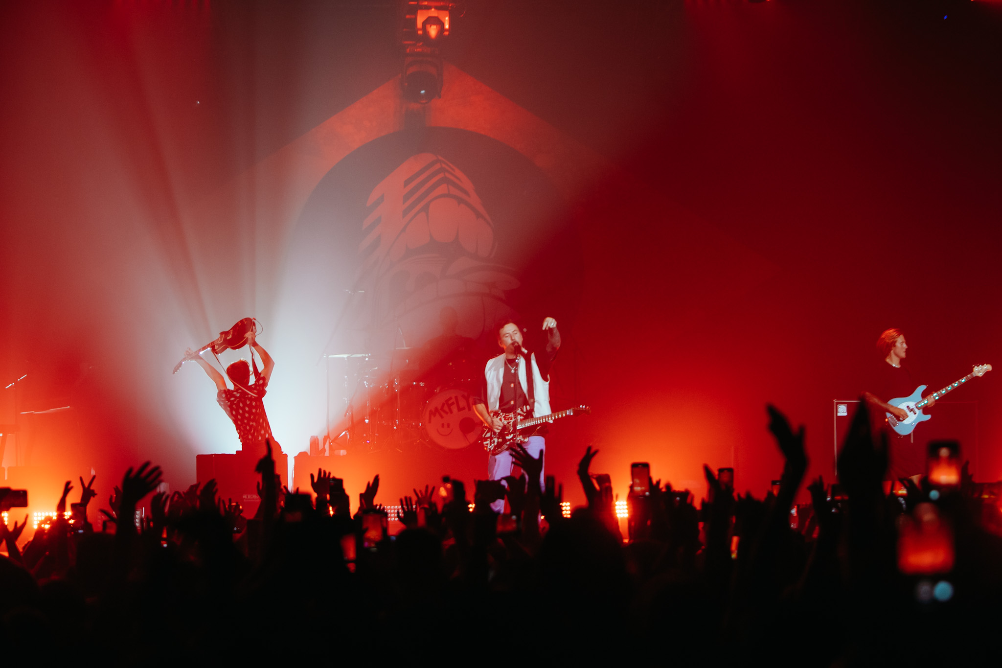 McFly em show em São Paulo. Foto mostra o público, luzes vermelhas e os integrantes da banda ao fundo