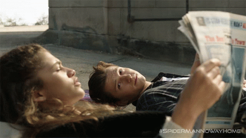 Zendaya lendo jornal e Tom Holland deitado em cena de Homem-Aranha