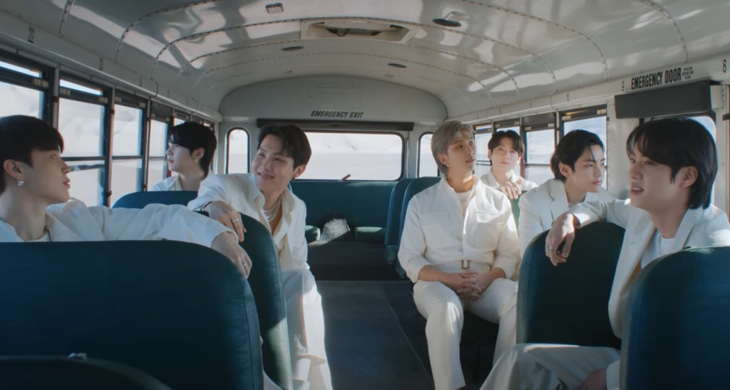 BTS em Yet To Come; eles estão sentados em um ônibus sorrindo