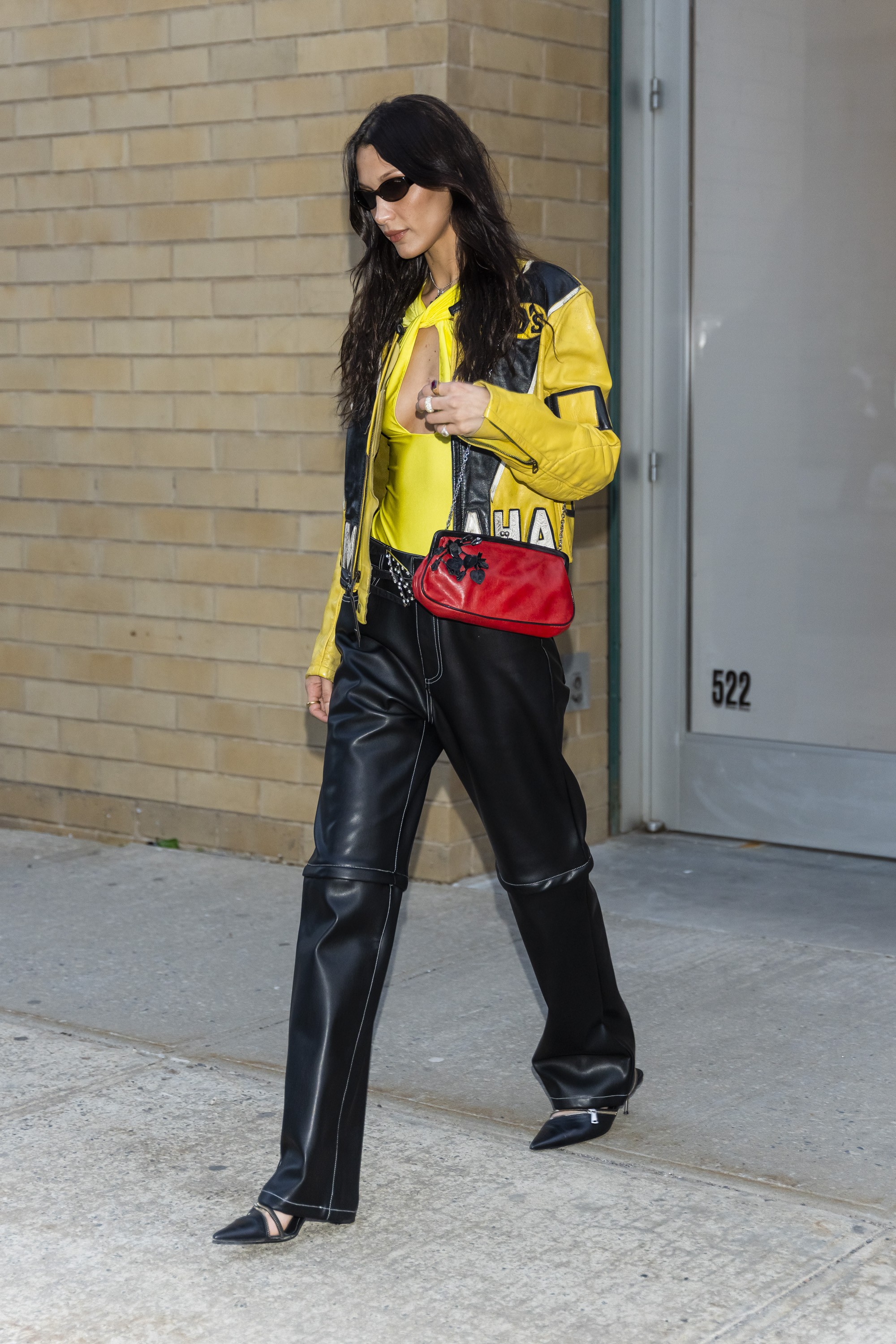 Bella Hadid usando look com referências da estética bikercore com jaqueta de couro amarela e preta, calça de couro e bolsa vermelha