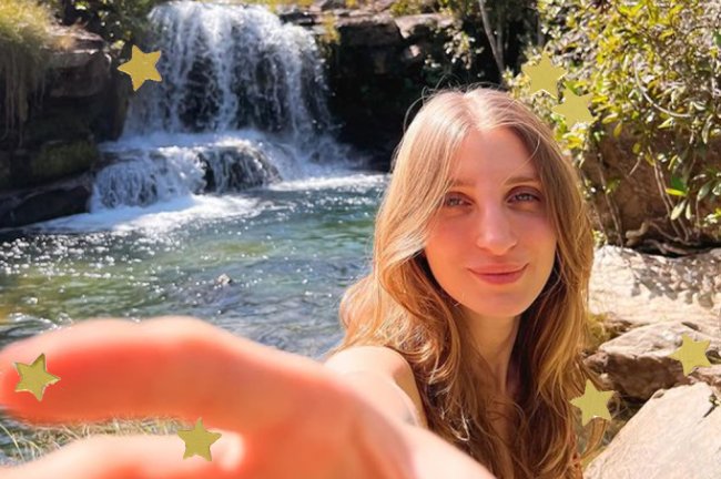 Foto de Gabie Fernandes na cachoeira. Ela é uma mulher branca e loira, e sorri com os olhos