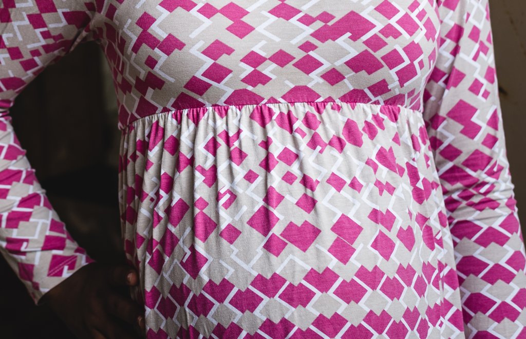 Foto da barriga de uma adolescente grávida. Ela usa uma blusinha solta rosa bebê de formas geométricas pink