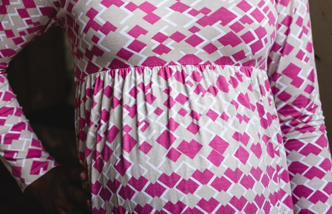 Foto da barriga de uma adolescente grávida. Ela usa uma blusinha solta rosa bebê de formas geométricas pink