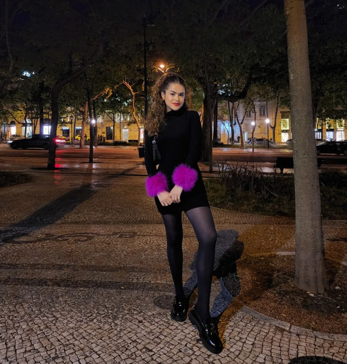 Maisa Silva usando vestido preto com mangas de pelinhos roxos, meia-calça preta e mocassim preto